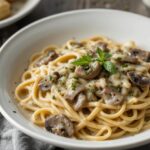 A bowl of creamy mushroom pasta with milk, garnished with herbs.